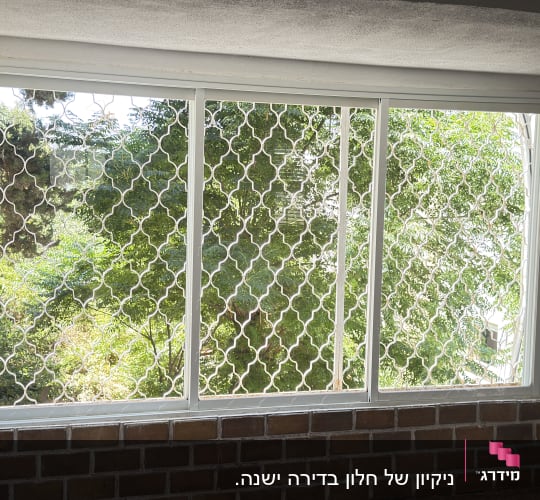 חלון עם סורגי מתכת ונוף עצים בחוץ
